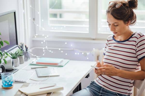 woman in striped shirt plans her week at white desk with computer and papers