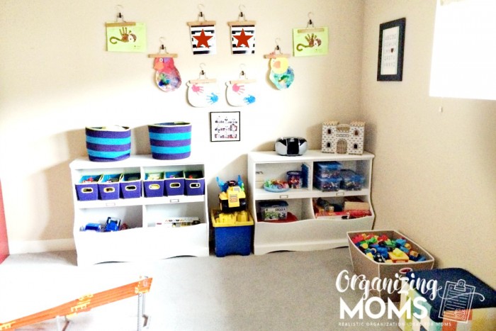 Playroom organization with white shelves filled with toys and artwork on walls