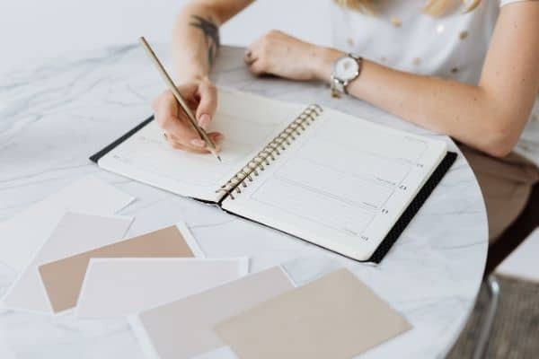 productive mom writing in planner wearing watch at marble table