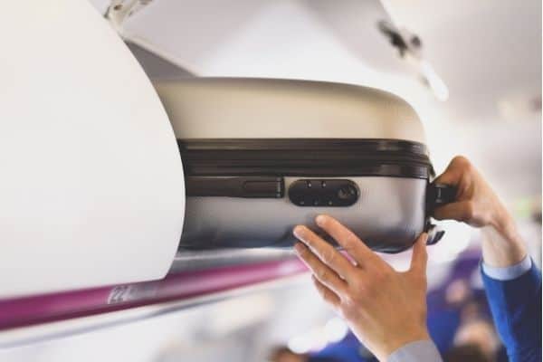 man putting carry on suitcase in overhead compartment in airplane
