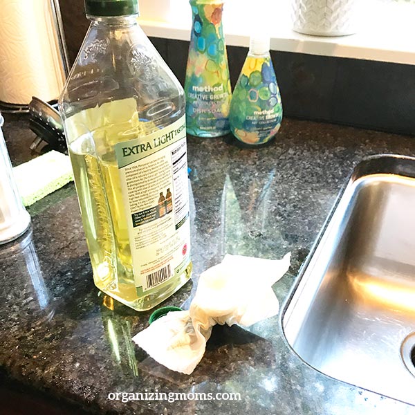 A bottle olive oil next to sink. Paper towel with oil residue.