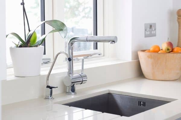 stainless sink white countertops in front of window bowl of oranges