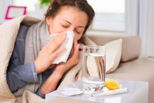 A sick mom blowing her nose. Glass of water, half a lemon.