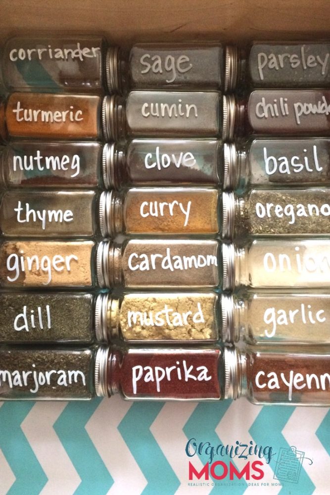 A close up filled square spice bottles labeled with white chalk marker on blue and white chevron patterned shelf liner