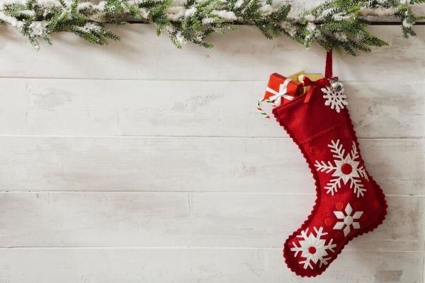 red stocking filled with small gift, garland above, on white background