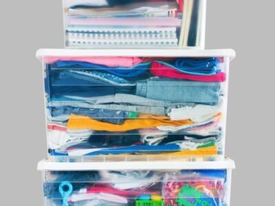 organizing products that are clear storage bins filled with clothes notebooks toys on gray background