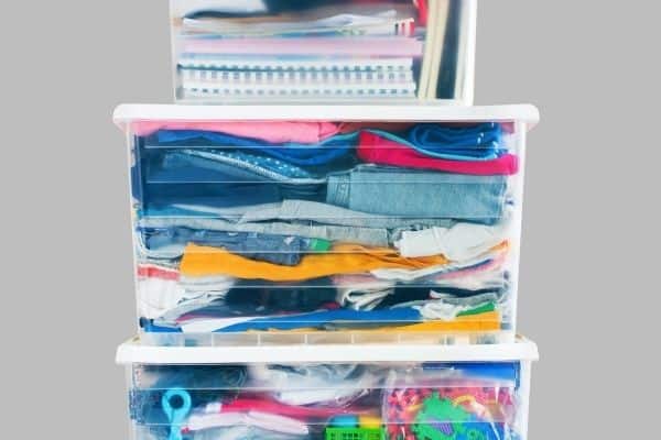 organizing products that are clear storage bins filled with clothes notebooks toys on gray background