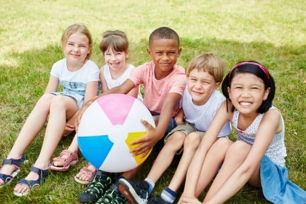 5 children sitting in grass posing with beach ball to symbolize planning ahead for summer