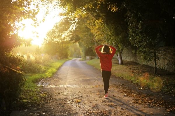 woman walking on dirt road with sun rising to symbolize how to get to 10000 steps a day