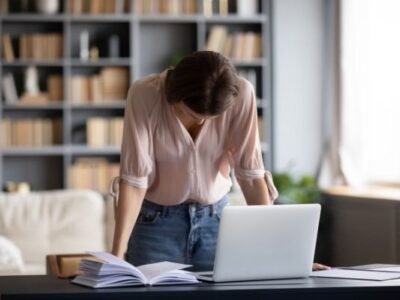 overwhelmed mom with head down in front of laptop bookcases in background