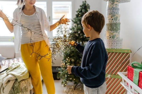 boy and mom decorating christmas tree and untangling christmas lights