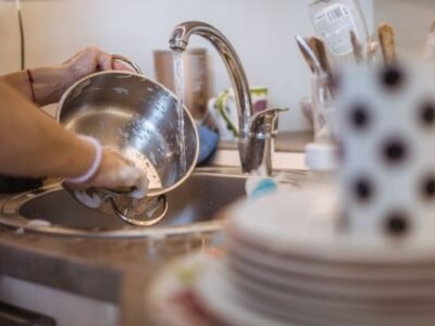 stack of dishes by sink someone washing a pot