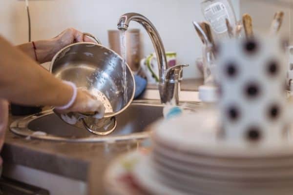 stack of dishes by sink someone washing a pot