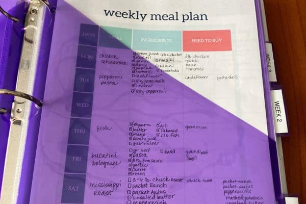 Weekly meal plan printable that shows meals, ingredients, and need to buy columns. In meal plan binder with purple divider pocket.