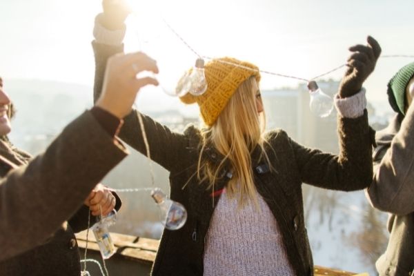 woman in yellow hat preparing for the holidays by hanging lights outside