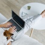 woman on laptop with dog sitting next to her, feet on white coffee table